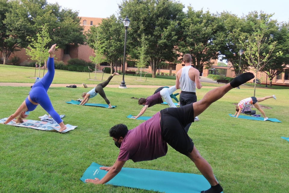 Students move into a leg lifted pose at a SLU STEM Wellness outdoor yoga session.