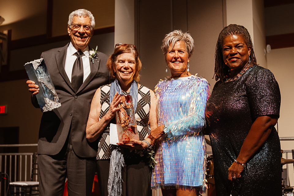 A man and woman proudly display two awards, accompanied by two women, all smiling together in celebration.