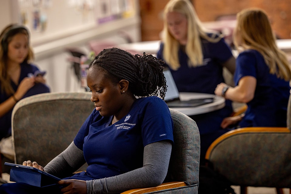 A nursing student in scrubs looks at a tablet while studying