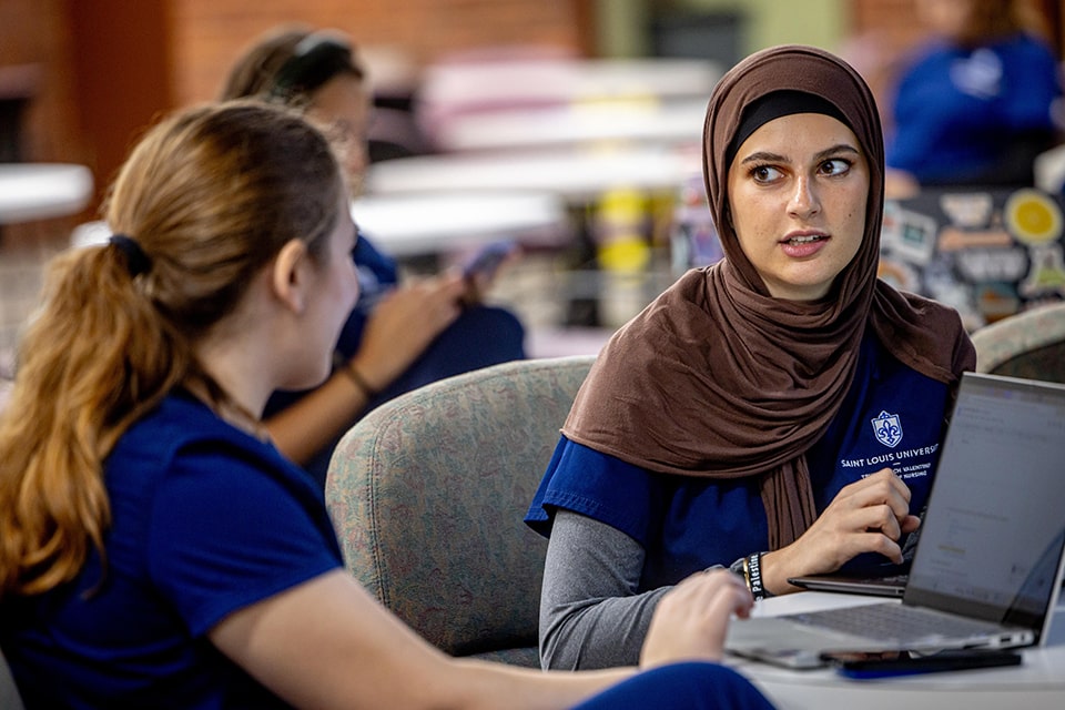 Two students have a discussion while sitting in a study area.