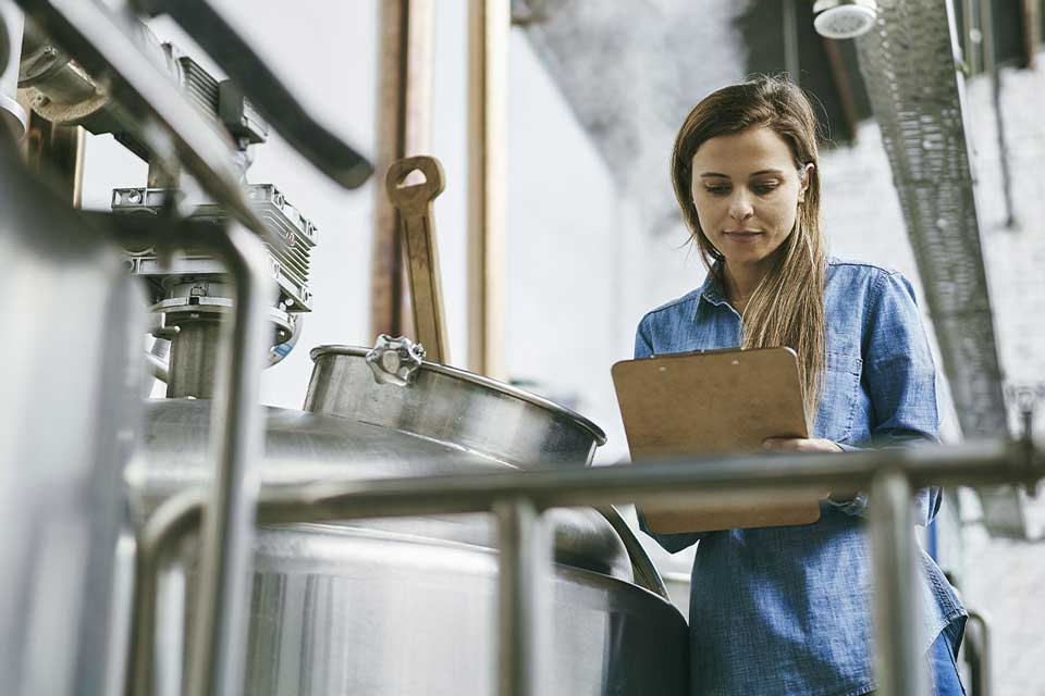 Women with clipboard near brewing equiptment
