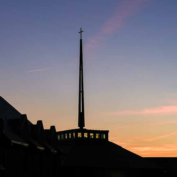 The spire of SLU’s Jesuit Center seen at dusk with the setting sun behind it.