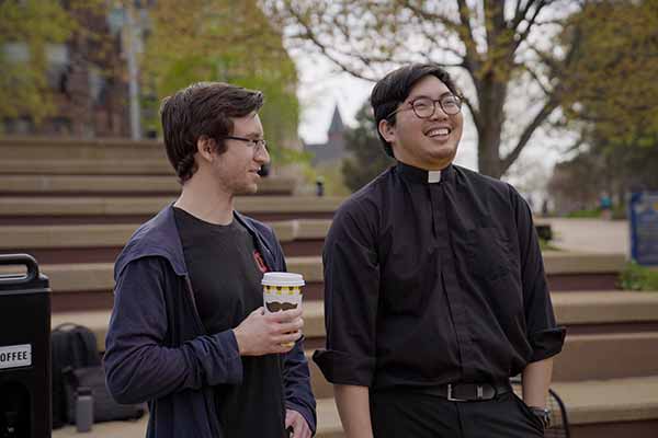 A young Jesuit laughs while chatting with another young man in the plaza of the clock tower.