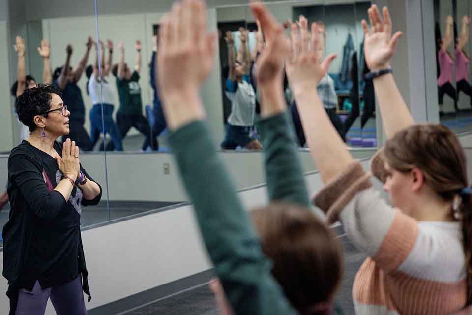 A teacher leading a yoga class in front of a mirror with students facing her