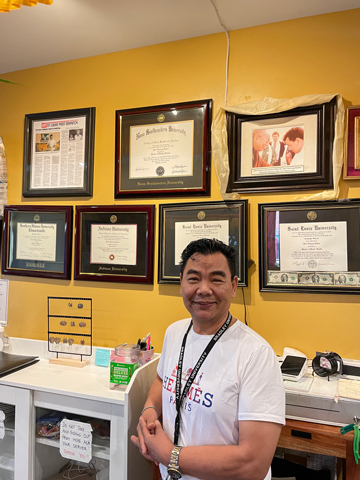 Devi States, PhD, DHSc, MPH, MSW, MS poses with his degrees that are proudly displayed on the wall at Everest Cafe.