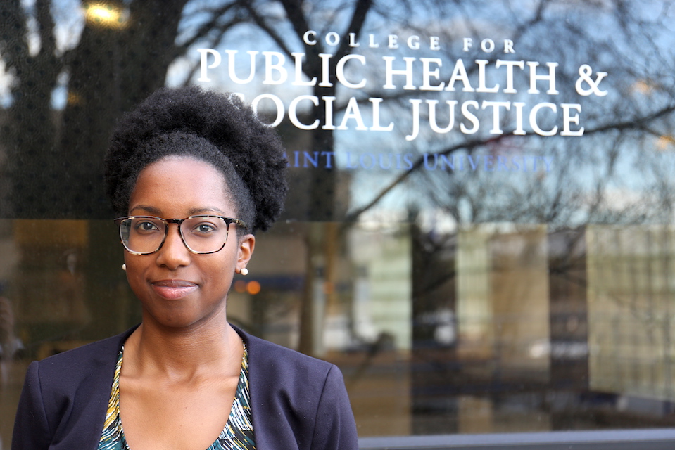 Brianna Clare stands in front of the entrace to Saint Louis University's College for Public Health and Social Justicealth and