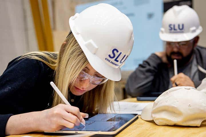 A student wearing a hardhat works on a tablet in a SLU classroom.