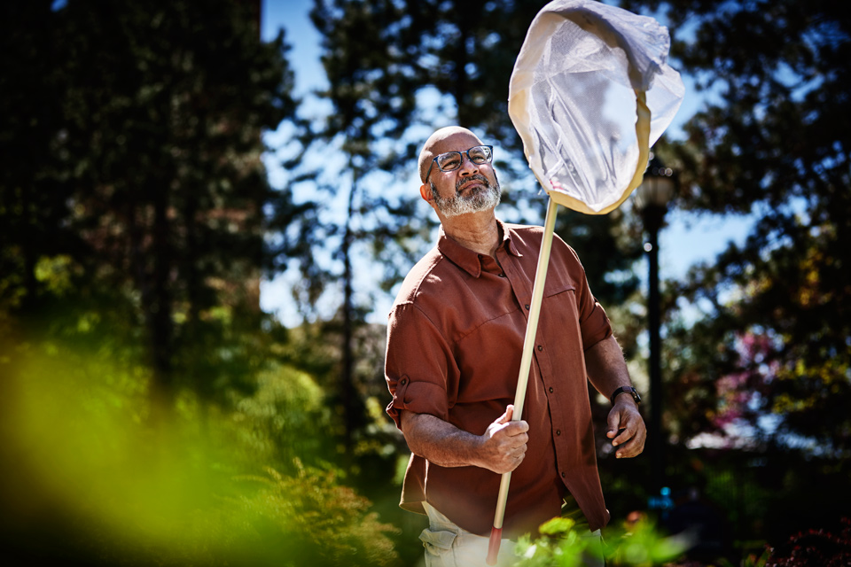 Gerardo Camilo, Ph.D. using a net outdoors to catch insects.