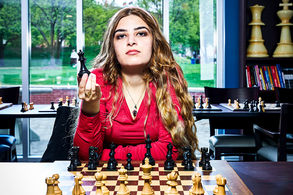 Chess grandmaster Dorsa Derakhshani sits at a chess board, holding a piece.