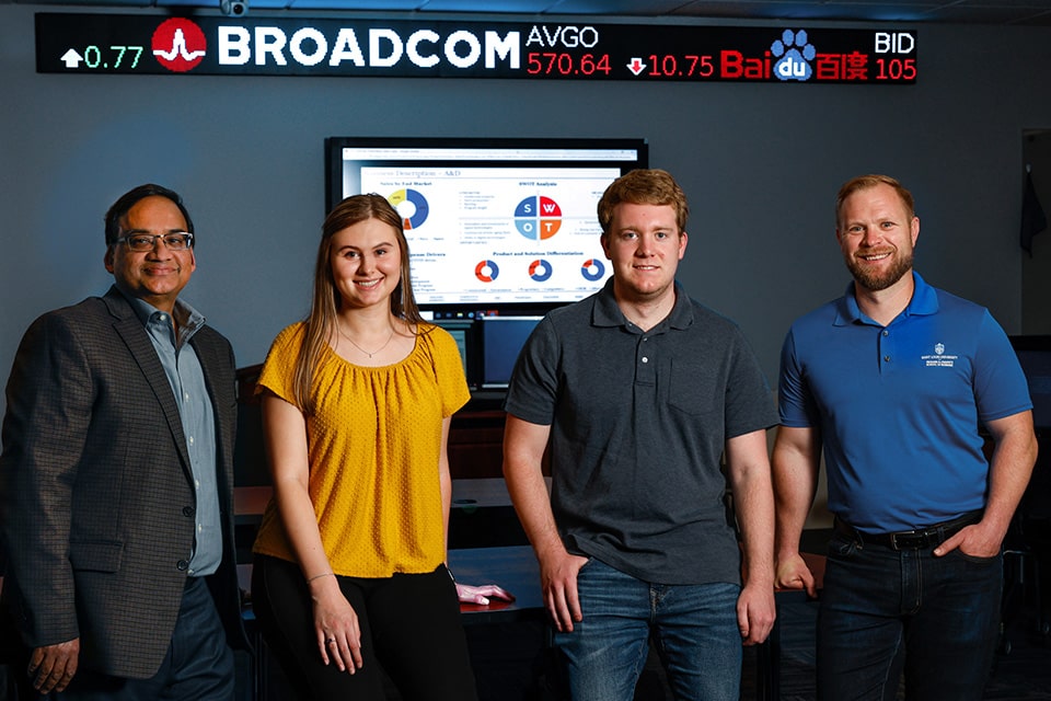 Bansal, Pezold, Dowell and Doellman pose in front of a ticker screen